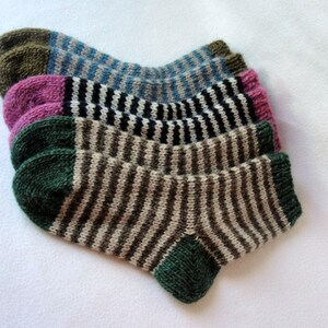 K&ouml;nnte beinhalten: Vier Paar gestreifte Stricksocken in verschiedenen Farben, darunter Gr&uuml;n, Braun, Schwarz, Wei&szlig;, Rosa und Blau. Die Socken sind gefaltet und &uuml;bereinander gestapelt.