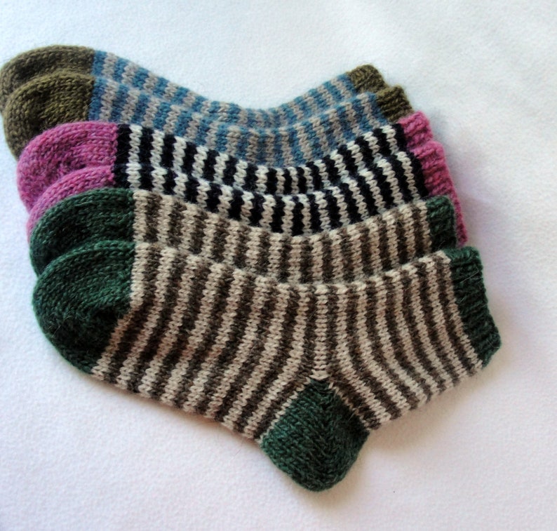 K&ouml;nnte beinhalten: Vier Paar gestreifte Stricksocken in verschiedenen Farben, darunter Gr&uuml;n, Braun, Schwarz, Wei&szlig;, Rosa und Blau. Die Socken sind gefaltet und &uuml;bereinander gestapelt.