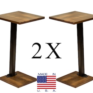 May include: Two tall side tables featuring square wooden tops with a medium brown finish, supported by single black metal vertical posts and square wooden bases. The text 2X is centered between the tables, with a Made in U.S.A. flag icon below.