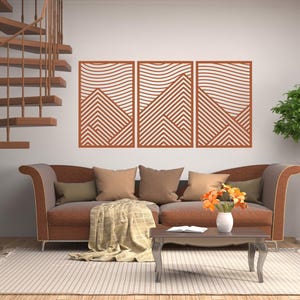 May include: A living room scene featuring a brown sofa with throw pillows and a blanket. Above the sofa are three matching geometric wall art pieces. A spiral staircase and a potted plant are also visible. The room has a neutral color palette.