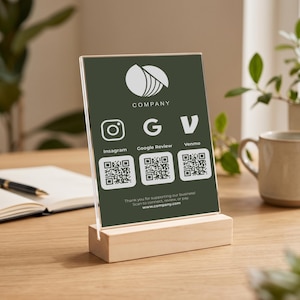 May include: A vertical acrylic sign with a dark green background held by a light wood base. It features a white logo, the text COMPANY, and three white icons for Instagram, Google Review, and Venmo, each with a corresponding QR code below.