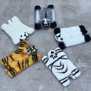 May include: A collection of five felt animal figures: a white polar bear, a gray panda, a white panda, a yellow and black tiger, and a white and black ghost. Each figure is lying down, with detailed facial features.