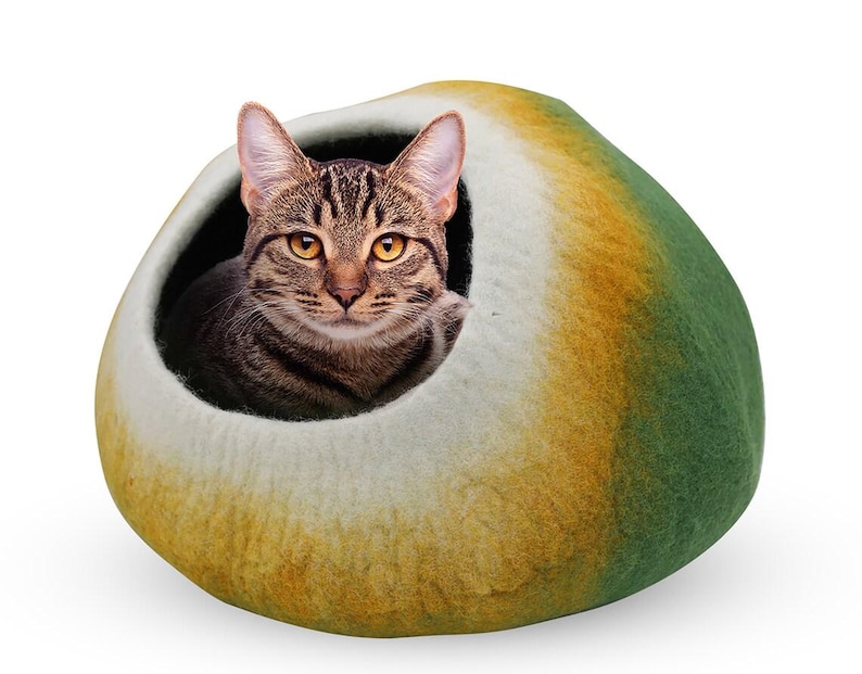 May include: A tabby cat peeks out from a cozy, enclosed cat bed. The bed is a rounded shape, with a color gradient of green, yellow, and white. The cat's fur is brown and black, and its eyes are yellow.