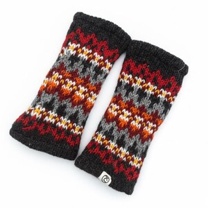 May include: A pair of knitted fingerless gloves in a fair isle pattern. The gloves feature a black cuff and a design of red, orange, gray, white, and yellow geometric shapes. A small white tag with a logo is visible on one glove.