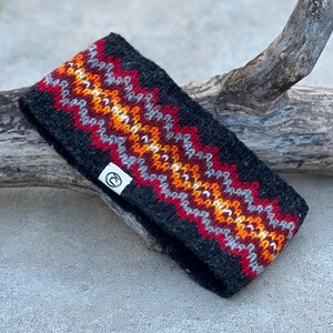 May include: A dark gray knit headband with a colorful zigzag pattern in red, orange, yellow, and gray. The headband has a small white tag with a logo. The accessory is designed to keep the ears warm.