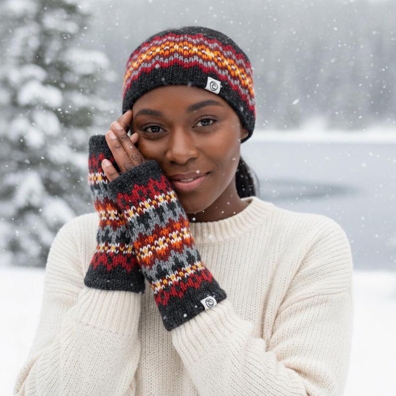 May include: A knitted winter hat and fingerless gloves set. The hat and gloves feature a geometric pattern in red, orange, gray, and black. The woman in the image is wearing a cream-colored sweater.