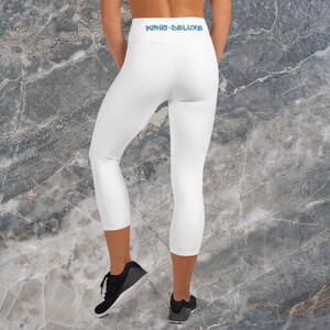 Könnte beinhalten: Weiße Capri-Leggings mit dem Text "KIRIN-DELUXE" in Hellblau am hinteren Bund. Die Leggings sind am Wadenbereich geschnitten. Die Person trägt schwarze Sportschuhe. Marmorierter Hintergrund.