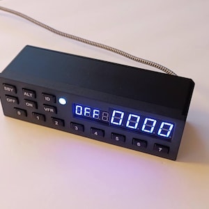 May include: A black rectangular aviation transponder control unit featuring a digital display with blue illuminated numbers, a row of numbered buttons from 0 to 7, and additional function buttons labeled SBY, OFF, ALT, ON, ID, and VFR.