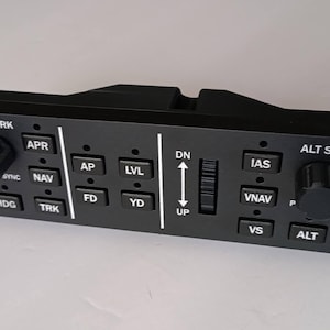 May include: A black flight control panel featuring two rotary knobs and multiple square push buttons labeled HDG/TRK, APR, SYNC, NAV, HDG, TRK, AP, LVL, FD, YD, DN, UP, IAS, VNAV, VS, ALT SEL, and ALT. The rectangular unit is secured with four silver screws.