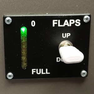 May include: A black control panel with the text "FLAPS" and "FULL". A green light indicates the flaps are at zero. A white switch is in the "UP" position. Four screws secure the panel.