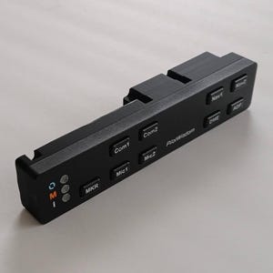 May include: A black rectangular aviation audio control panel featuring labeled buttons for Com1, Com2, Mic1, Mic2, MKR, Nav1, Nav2, DME, and ADF. The unit includes the text PilotWisdom and a vertical column of three small circular indicator lights.