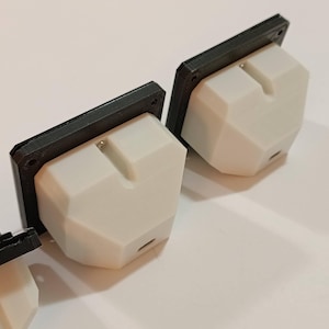 May include: Three white, geometric-shaped electrical outlets with black rectangular faceplates. The outlets have a small, rectangular slot and a small port on the bottom. The objects are on a white surface.