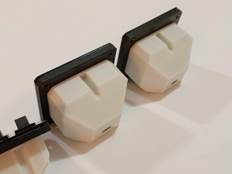 May include: Three white, geometric-shaped electrical outlets with black rectangular faceplates. The outlets have a small, rectangular slot and a small port on the bottom. The objects are on a white surface.