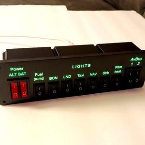 May include: A black rectangular aircraft switch panel featuring two red rocker switches labeled Power ALT BAT and eight black rocker switches labeled Fuel pump, BCN, LND, Taxi, NAV, Strb, Pitot heat, and AvBus 1 2, all with illuminated green text.