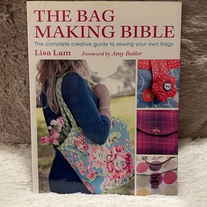 Può includere: La copertina del libro The Bag Making Bible presenta una donna che tiene una borsa a tracolla floreale. La copertina include anche immagini di altre borse, tra cui una borsa rossa con un abbellimento floreale, una borsa a quadri e una borsa a pois.