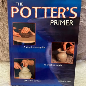Könnte beinhalten: Der Einband des Buches The Potter's Primer zeigt einen blauen Hintergrund mit dem Titel in weißer und roter Schrift. Drei Bilder zeigen Hände, die mit Ton auf einer Töpferscheibe arbeiten, um eine Schüssel, eine Vase und einen Deckeltopf zu erstellen.