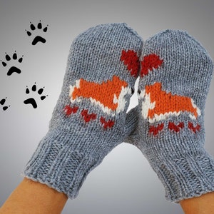 Könnte beinhalten: Ein Paar graue Strickhandschuhe mit orangefarbenen und weißen Fuchsdesigns. Die Handschuhe werden von den Händen einer Person getragen.