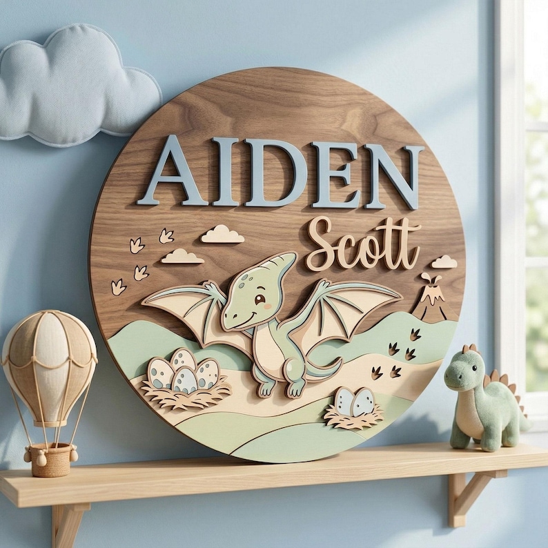 May include: A round wooden sign with the name "AIDEN Scott" in blue and beige lettering. The sign features a 3D design of a cartoon dinosaur, eggs, and a volcano. A plush dinosaur and hot air balloon are on a shelf below.