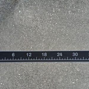 Pode incluir: Uma r&eacute;gua preta com marca&ccedil;&otilde;es e n&uacute;meros brancos, medindo at&eacute; 91 cm. A r&eacute;gua tem incrementos marcados a cada cent&iacute;metro, com n&uacute;meros maiores a cada 15 cm. A r&eacute;gua &eacute; retangular e est&aacute; sobre uma superf&iacute;cie cinza.
