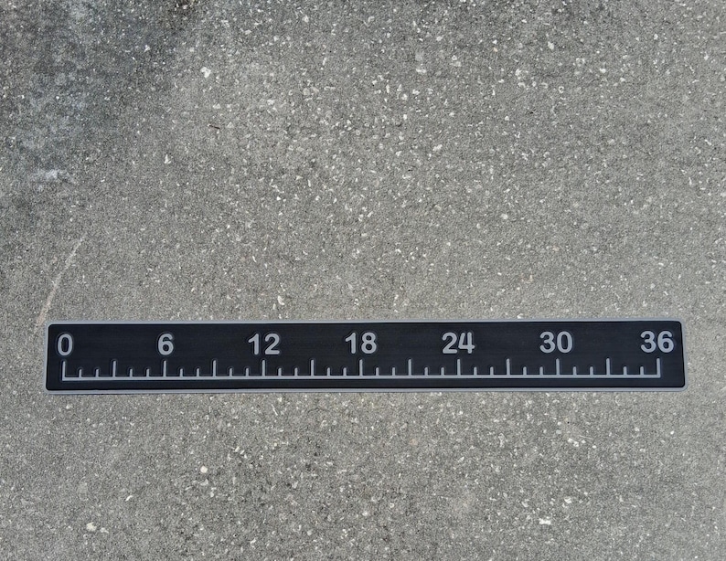 Pode incluir: Uma r&eacute;gua preta com marca&ccedil;&otilde;es e n&uacute;meros brancos, medindo at&eacute; 91 cm. A r&eacute;gua tem incrementos marcados a cada cent&iacute;metro, com n&uacute;meros maiores a cada 15 cm. A r&eacute;gua &eacute; retangular e est&aacute; sobre uma superf&iacute;cie cinza.