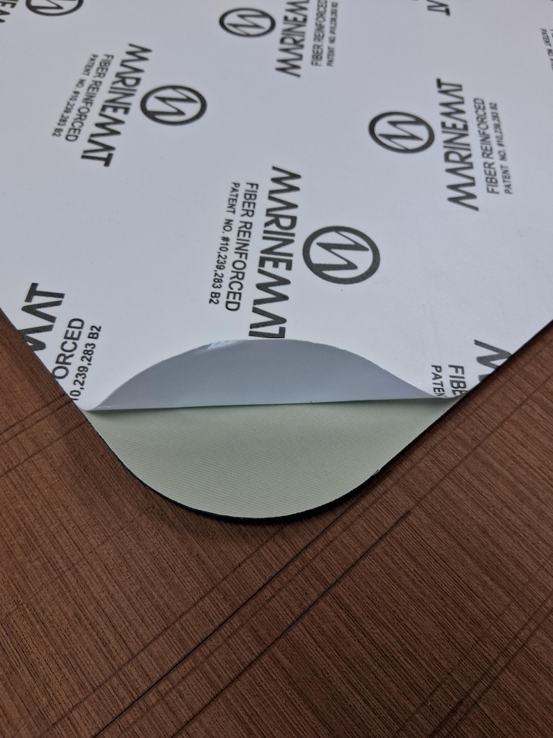 Puede incluir: Una l&aacute;mina parcialmente despegada de material Marinemat reforzado con fibra. La capa superior es blanca con texto negro y un logotipo. La capa inferior expuesta es de color verde claro. El material est&aacute; sobre una superficie marr&oacute;n texturizada.
