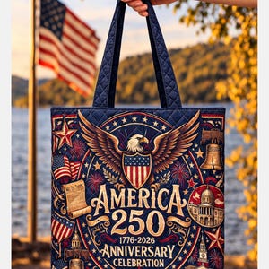 Peut inclure: Un sac fourre-tout bleu marine avec un motif matelassé et des poignées. Le sac présente un motif patriotique avec un aigle, le drapeau américain et le texte "America 250 Anniversary Celebration 1776-2026".