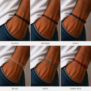 May include: A collection of six bracelets in various colors: black, brown, navy, beige, grey, and dark red. Each bracelet features a double-strand design. The bracelets are displayed on a person's wrist, showcasing the different color options.
