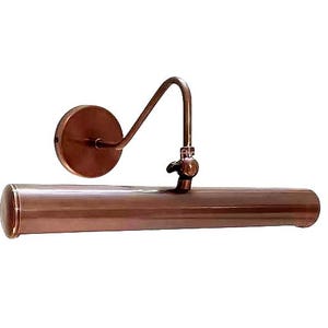 May include: A copper-colored picture light with a curved arm and a round wall mount. The cylindrical light fixture has rounded ends. The design is vintage and suitable for illuminating artwork or photographs.