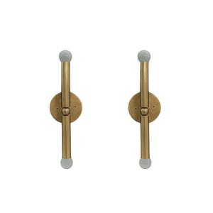 May include: Two brass wall sconces with a vertical design. Each sconce features a circular base, a central vertical rod, and a small, frosted glass globe at each end. The sconces are designed for wall mounting.