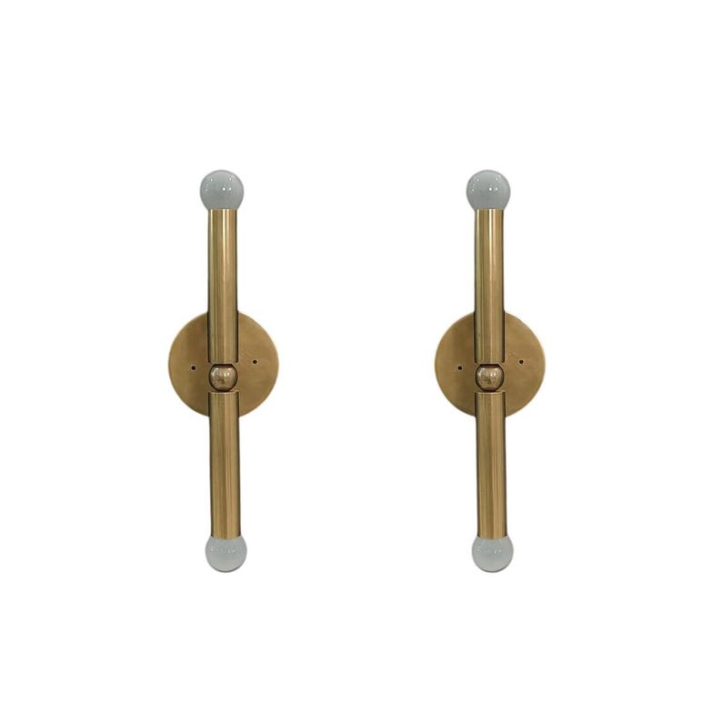 May include: Two brass wall sconces with a vertical design. Each sconce features a circular base, a central vertical rod, and a small, frosted glass globe at each end. The sconces are designed for wall mounting.