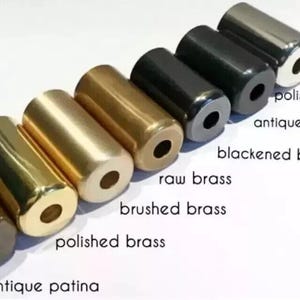 May include: A collection of cylindrical metal objects in various finishes, including polished chrome, antique black, and polished brass. The image displays the names of each finish. The objects are arranged in a row against a white background.