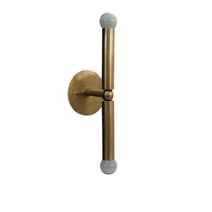 May include: A brass-colored wall sconce with a circular base and two vertical rods. Each rod has a white, spherical light at the end. The sconce is designed to be mounted on a wall and provides upward and downward lighting.