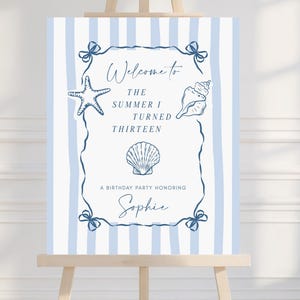 May include: A welcome sign on an easel with a blue and white striped background. The sign has a decorative border with a starfish, seashell, and scallop shell illustration. Text reads "Welcome to The Summer I Turned Thirteen" and "A Birthday Party Honoring Sophie."