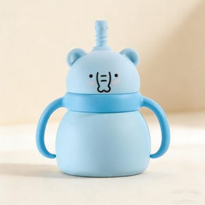 May include: A light blue baby sippy cup with a bear face design. The cup has a straw, two handles, and a blue band around the middle. The bear face has black eyes and a smiling mouth. The cup is designed for easy gripping.