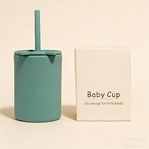 May include: A teal silicone baby cup with a matching straw and lid, next to a cream-colored box. The box has the words "Baby Cup" and "Silicone cup for little hands" printed on it.
