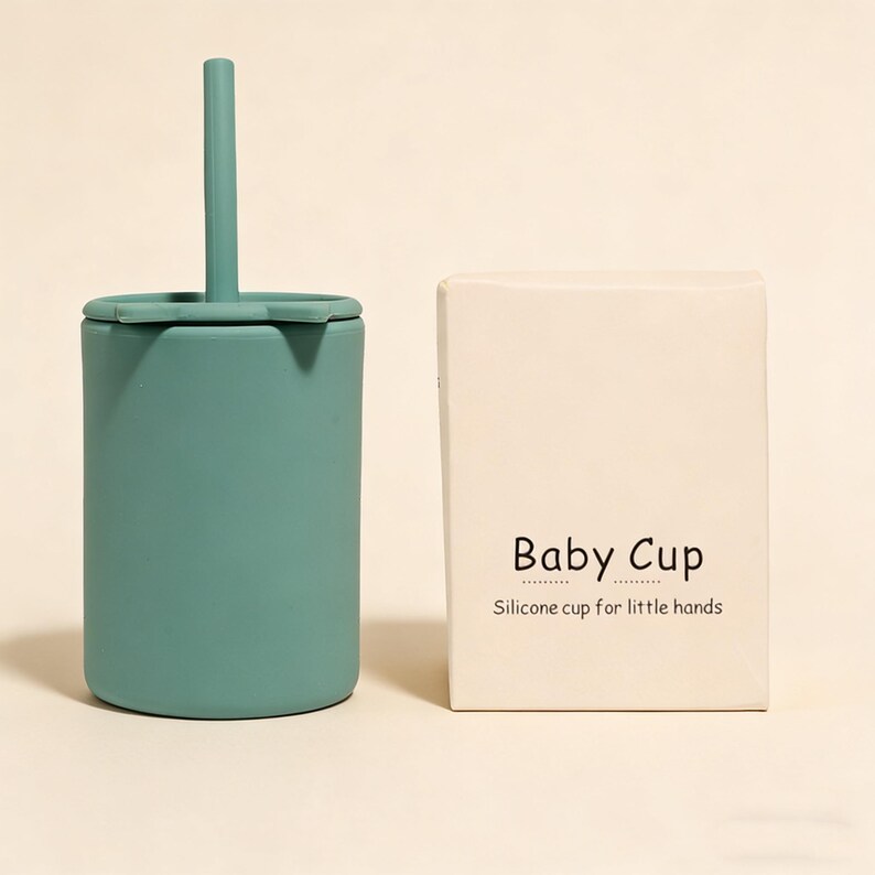 May include: A teal silicone baby cup with a matching straw and lid, next to a cream-colored box. The box has the words "Baby Cup" and "Silicone cup for little hands" printed on it.