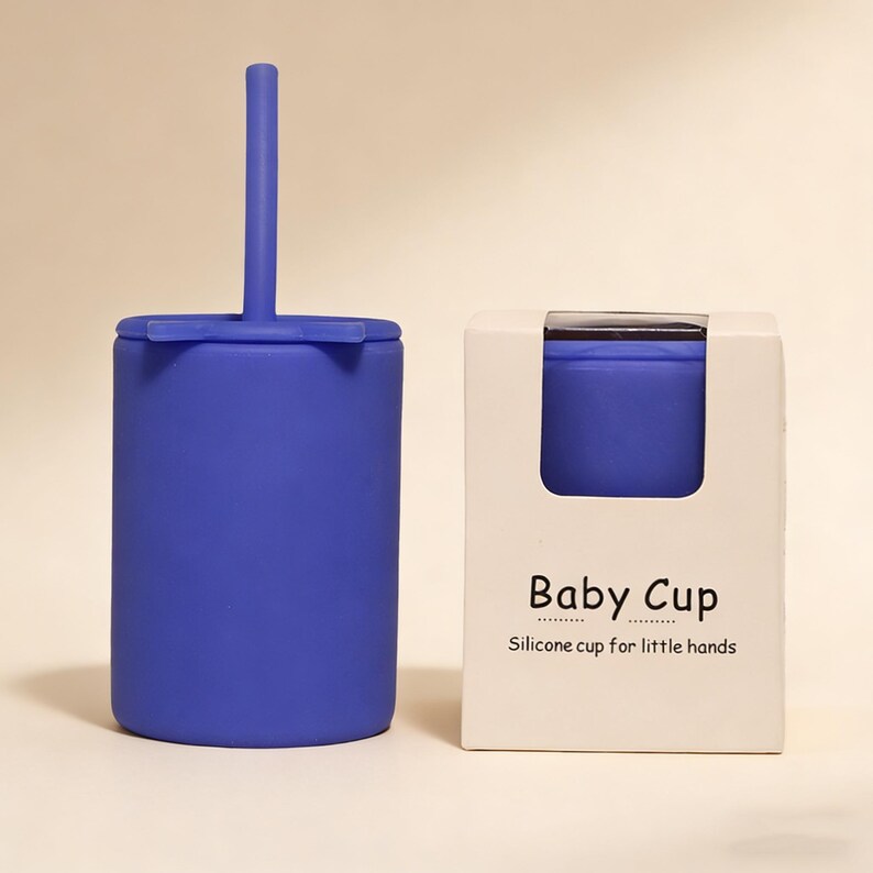 May include: A blue silicone baby cup with a matching straw and lid. The cup is next to a white box with the text "Baby Cup" and "Silicone cup for little hands."