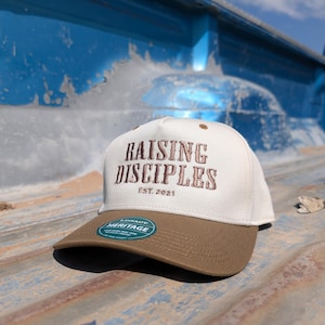 以下が含まれることがあります： 前面に「RAISING DISCIPLES EST. 2021」の文字が刺繍された、白と茶色の野球帽。 茶色のつばとレガシーヘリテージタグが付いています。
