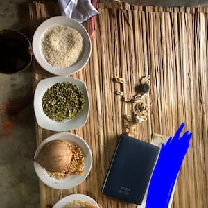 Puede incluir: Vista aérea de varios granos y semillas en cuencos blancos sobre una estera tejida. Incluye arroz, lentejas verdes, maíz y una calabaza. También hay un cuaderno azul y una pequeña pila de semillas.