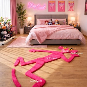 Puede incluir: Un dormitorio rosa con una cama grande, ropa de cama rosa y una alfombra rosa. Una alfombra con forma de pantera rosa está en el suelo de madera. La pared tiene un letrero de neón que dice "Stay Cool" y obras de arte enmarcadas. También hay dos mesitas de noche con lámparas.