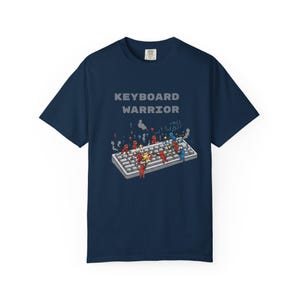 May include: Navy blue t-shirt with the text "KEYBOARD WARRIOR" above a graphic of a keyboard with cartoon figures engaged in battle. The design features red, blue, and yellow characters, suggesting a gaming or tech theme.