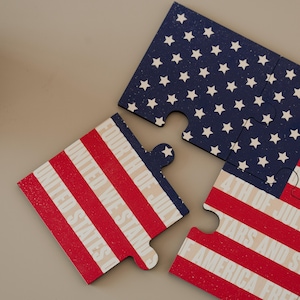 Peut inclure: Puzzle de quatre pièces avec un motif de drapeau américain. Les pièces présentent des rayures rouges et blanches et un champ bleu avec des étoiles blanches. Le texte comprend "UNITED STATES" et "4TH OF JULY".