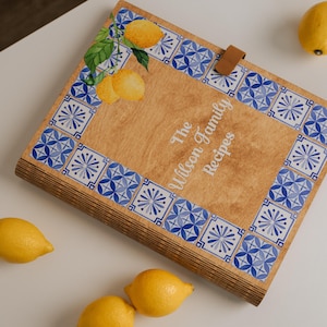 Könnte beinhalten: Holzrezeptordner mit einer Zitronen- und Blattillustration und einem blau-weißen Kachelrand. Auf dem Cover steht "The Wilson Family Recipes". Mehrere Zitronen sind um den Ordner herum verstreut.