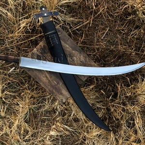 Puede incluir: Una espada de acero curvada con mango de madera marrón oscuro y una funda de cuero negro a juego. La hoja presenta un acabado metálico pulido y una curva distintiva, mientras que la funda incluye una guarda en forma de cruz y cordones.