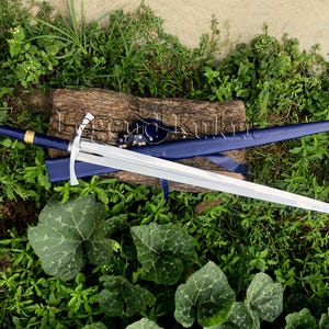 May include: A longsword with a polished steel blade, a crossguard, and a blue leather-wrapped hilt featuring a gold-colored ring. The sword is accompanied by a matching blue scabbard with a metallic tip, displaying the text Legend Kukri.