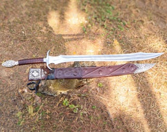 May include: A silver-colored metal sword with a curved blade and a brown leather-wrapped handle. The sword features an ornate silver pommel and crossguard. It is accompanied by a matching brown leather scabbard with silver metal accents.