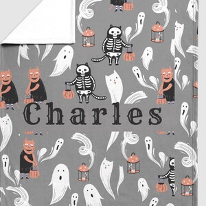 May include: A gray Halloween-themed blanket featuring a repeating pattern of ghosts, cats in skeleton costumes, and devilish characters carrying lanterns and pumpkins. The name "Charles" is printed in large letters across the center.