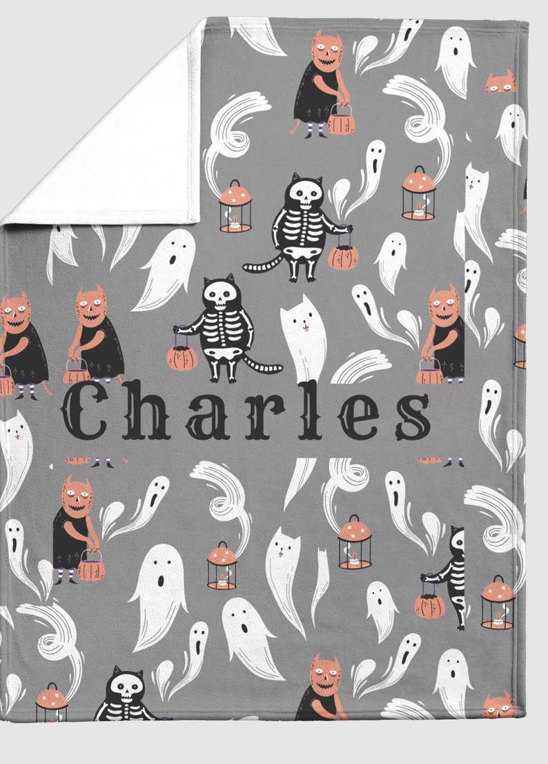 May include: A gray Halloween-themed blanket featuring a repeating pattern of ghosts, cats in skeleton costumes, and devilish characters carrying lanterns and pumpkins. The name "Charles" is printed in large letters across the center.