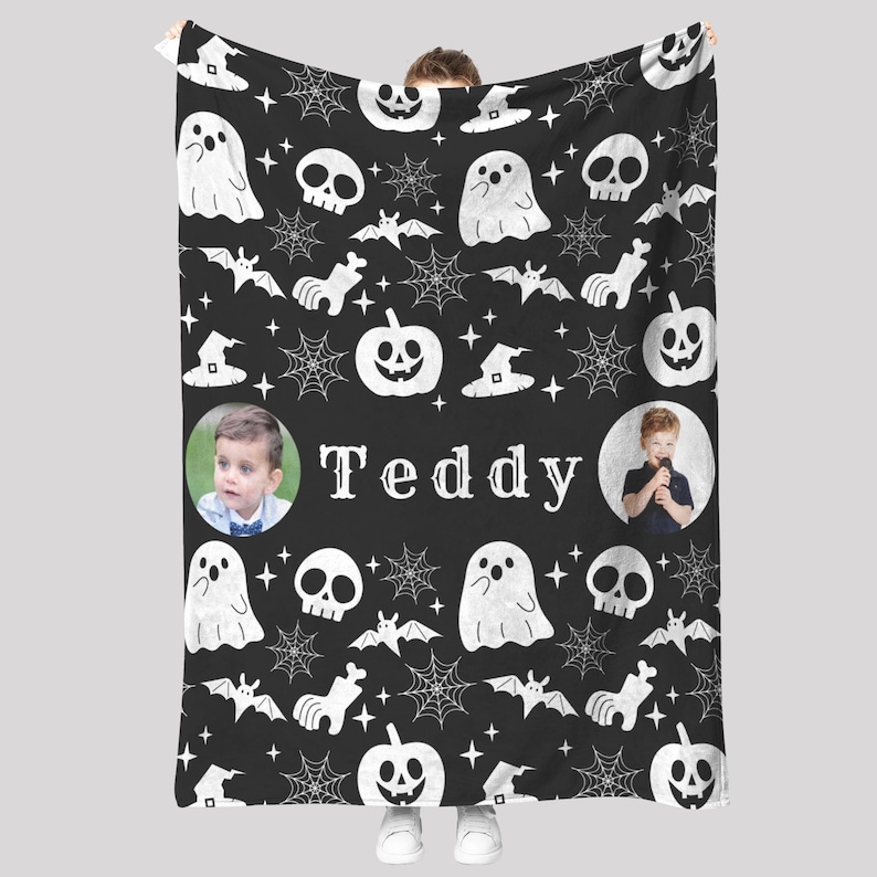 May include: Black Halloween-themed blanket with white ghost, skull, bat, pumpkin, and spiderweb patterns. The name "Teddy" is centered, with two circular photo inserts. A cozy, personalized gift.