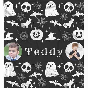 May include: Black Halloween-themed blanket with a repeating pattern of white ghosts, skulls, bats, spiderwebs, witch hats, and pumpkins. The name "Teddy" is centered in white text, with two circular photos of a child on either side.